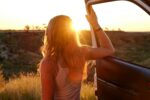 Woman holding vehicle door open looking into the sun